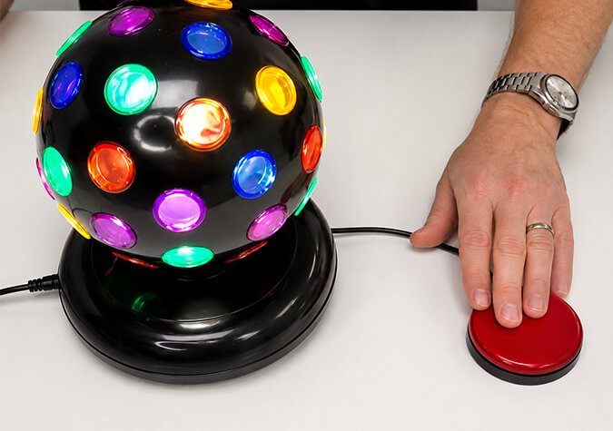 Colorful disco ball with a hand pressing a red Buddy Button IC Switch on a white surface