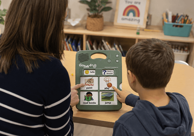 Teacher and student using a GoTalk 4+ Lite communication device in a classroom setting